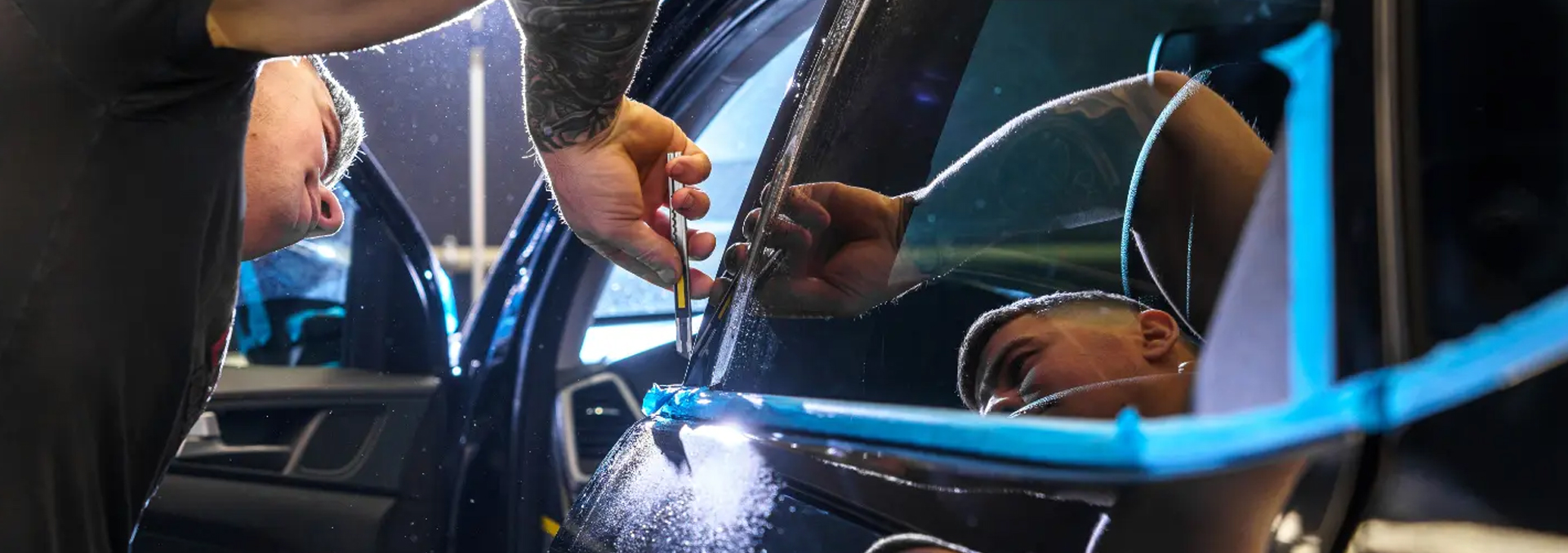 A man applying window tint film to a vehicle window in an auto shop.