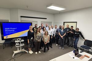 Group photo of UC Riverside's inaugural SBIR Phase I Workshop participants, instructors, and mentors standing together beside a presentation screen during the October 7, 2026 session.